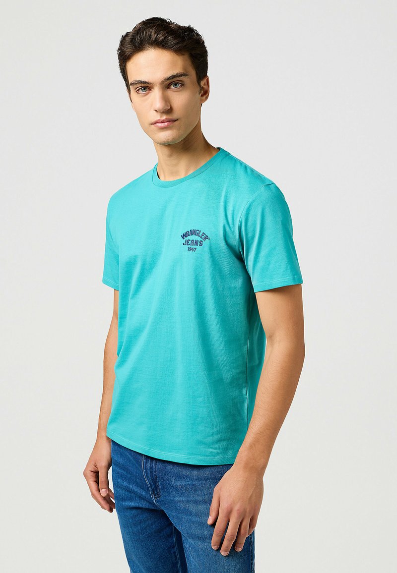 Turkoois katoenen t-shirt met korte mouwen, ronde halslijn en een lichte pasvorm. Bevat een klein marineblauw logo op de borst.