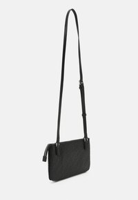 Černá crossbody taška s texturovaným logem, obdélníkový tvar, štíhlý design a nastavitelné rameno. Má zipové zapínání a kovové kování.