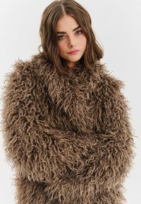 Hnědý kabát z umělé kožešiny s volnou, chlupatou strukturou a dlouhými rukávy, s vysokým límcem a uvolněným střihem.