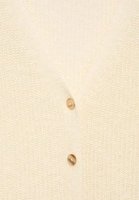 Tissu tricoté de couleur crème avec un col en V et deux boutons ronds marron visibles alignés verticalement.