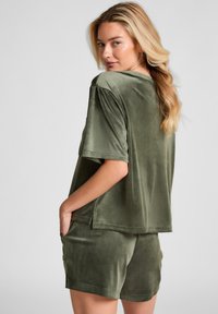Olijfgroene velours lounge-outfit bestaande uit een losse, kortärmelige top en bijpassende shorts met zijzakken en een zachte textuur.