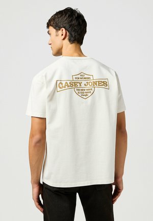T-shirt bianco in cotone con stampa grafica marrone sul retro, con il testo "CASEY JONES", logo e scollatura rotonda.