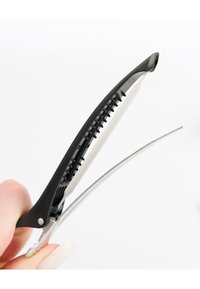 Svart plast hårklämma med en böjd design, utrustad med en silverfärgad metallfjäder och texturerat grepp för ett säkert fäste.