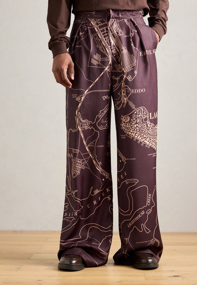 Pantalones de pierna ancha en tela de color marrón oscuro con un estampado de mapa en dorado que contrasta. Textura suave con detalles plisados y bolsillos laterales.