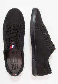 Schwarze Leinensneaker mit runder Spitze, schwarzer Gummisohle, Schnürdesign und einem gestreiften Akzent an der Zunge. Das Innenfutter verfügt über eine Markenkennzeichnung.