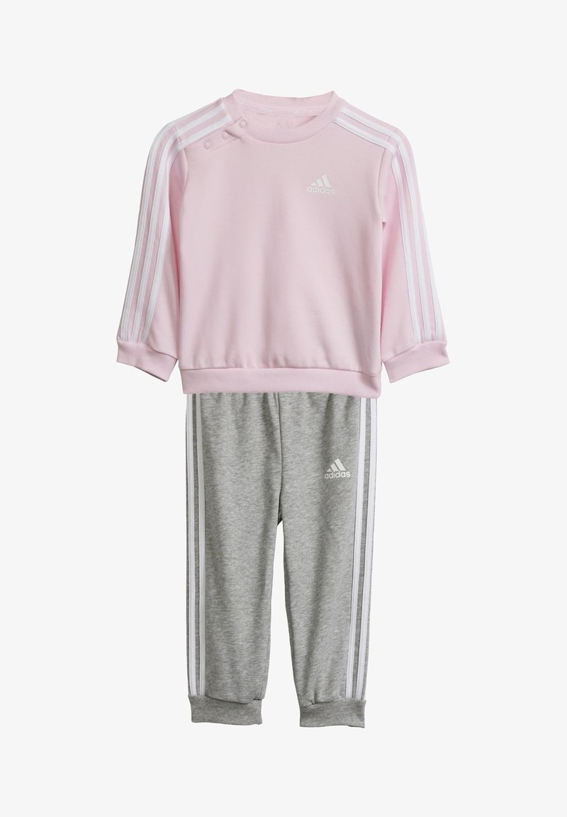 Sudadera rosa con rayas blancas y botones de presión, combinada con pantalones de chándal grises que tienen rayas laterales blancas y un logo. Tejido suave.