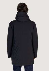 Cappotto imbottito nero con colletto alto e cappuccio, caratterizzato da una superficie esterna liscia e un orlo posteriore leggermente più lungo. Design semplice, senza ornamenti.