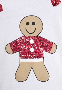 Bílá košile s grafikou perníkového mužíka, červeným flitrovým tričkem a černými konturami, s kulatou hlavou a usměvavým výrazem.