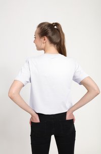 Camiseta blanca de algodón con mangas cortas, escote redondo y un corte holgado, combinada con jeans negros. El modelo posa con las manos en los bolsillos traseros.