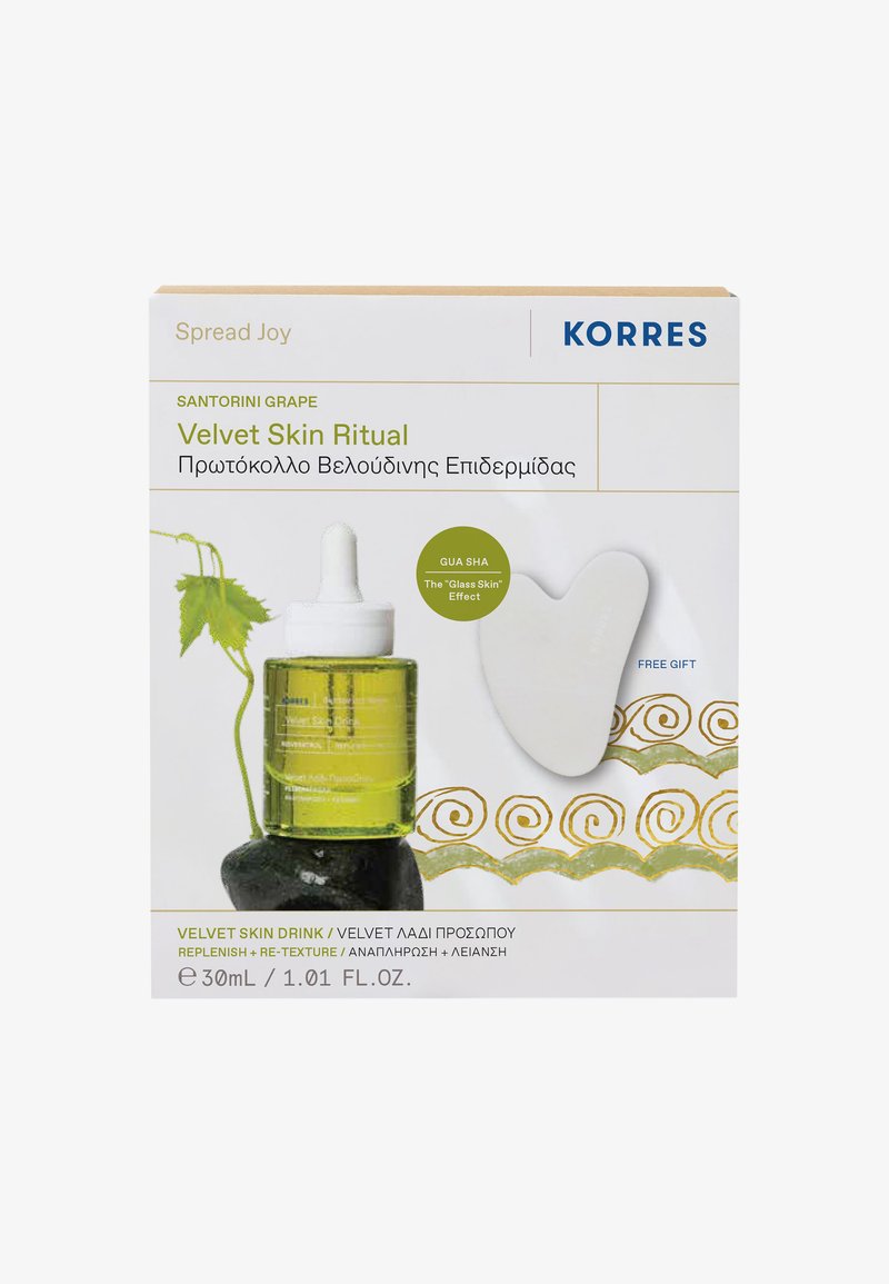 Botella de gotero de vidrio verde etiquetada como "Bebida de Piel de Terciopelo" con una herramienta gua sha blanca al lado. El envase presenta acentos dorados y gráficos en verde.