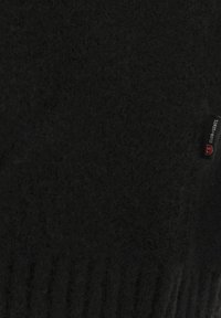 Schwarzer, weicher Stoff mit franjiertem Rand und einem kleinen eingenähten Etikett, auf dem "CLUB of GENTS" in weißer und roter Schrift zu lesen ist.