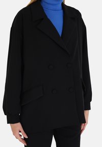 Zwarte dubbelzijdige blazer met een gestructureerde revers, twee voorzakken en knoopaccenten. De stof lijkt glad en inslag met een lichte textuur.