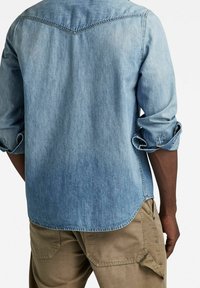 Lichtblauw spijkerhemd met opgerolde mouwen en een gebogen zoom. Heeft een schouderpasontwerp en stikseldetails. Draagt het met kaki broeken.