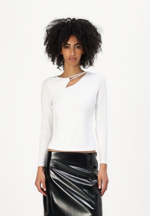White long-sleeve top with an asymmetrical neckline and a diagonal slash. Paired with a black high-gloss faux leather skirt.
