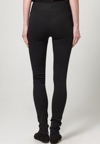 Zwarte legging met een brede tailleband, gladde stof, slanke pasvorm en ritsen bij de enkels, met een schone uitstraling en geen zichtbare patronen.