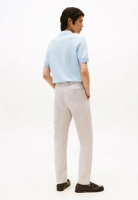 Polo a maglia azzurro chiaro con maniche corte, abbinato a pantaloni beige chiaro e mocassini marroni. Texture liscia, vestibilità casual.