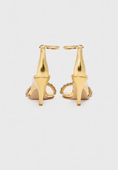 Sandali con tacco dorato e cinturini alla caviglia, design con punta aperta, finitura metallizzata lucida e dettagli decorativi lungo il tacco.