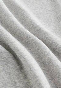 Soft light gray knit fabric with fine texture and gentle folds creating diagonal shadows.