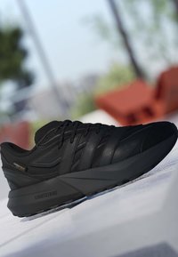 Sort atletisk sneakers med tekstureret overdel, snørelukning og tyk sål mærket "Lightstrike,", placeret udendørs på en hvid overflade.