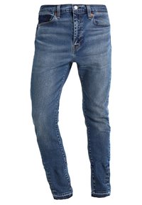 Vaqueros de mezclilla azul con corte ajustado, diseño de cinco bolsillos, cierre de botón y cremallera, y sutiles detalles desgastados en la tela.