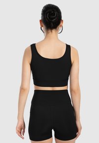 Top corto atlético negro con un escote redondeado y tirantes anchos, combinado con pantalones cortos negros de tiro alto que presentan una textura suave y un diseño ajustado.