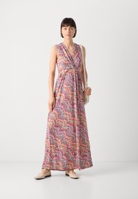 Robe maxi à motif de vagues colorées avec un décolleté en V plongeant, sans manches et taille cintrée. Associée à des chaussures beige clair.