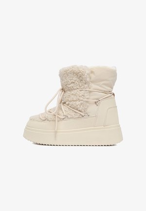 Cizme de iarnă bej cu talpă groasă, material pufos de blană de oaie pe partea din față, material neted pe partea din spate și detalii de șireturi încrucișate.