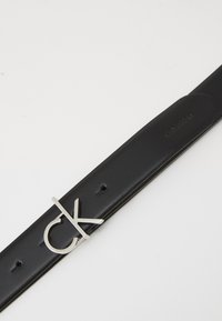 Must mustri nahkalt vöö, millel on hõbedane metallist "ck" klamber. Sile tekstuur ja minimalistlik disain. Reguleeritav mitme auguga.