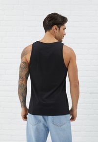 Canottiera nera senza maniche in cotone, caratterizzata da una texture morbida e un taglio rilassato, indossata con jeans in denim azzurro chiaro.