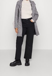 Grå texturerad kappa över en vit ribbad turtleneck, kombinerad med högmidjade svarta vida jeans och svarta platåboots.