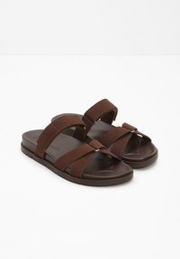 Sandales glissantes brunes avec deux sangles en tissu réglables et une semelle en caoutchouc texturée. Le design présente une esthétique minimaliste.