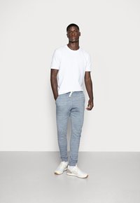 Camiseta blanca de cuello redondo combinada con pantalones de chándal gris claro y ajustados, con cordón. Llevado con zapatillas blancas, diseño sencillo.