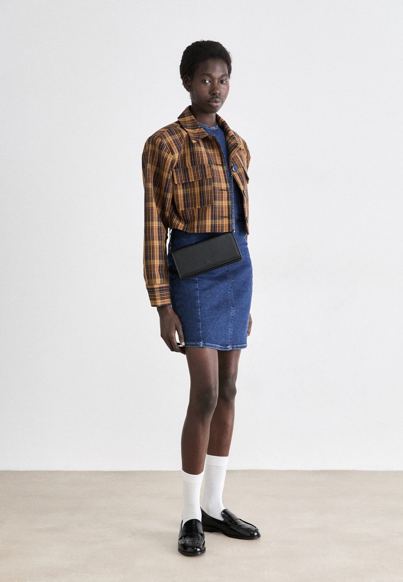 Giacca a quadri tagliata in arancione e marrone, abbinata a una gonna di jeans blu. Borsa a tracolla nera e mocassini neri completano il look. Calzini bianchi visibili.