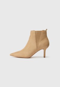 Beige mokkasini nilkkuri, jossa on terävä kärki, lyhyt stiletto-korko ja elastiset sivupaneelit helppoa pukeutumista varten. Sujuva pinta ja puhtaat muotoilulinjat.