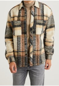 Wełniana marynarka w kratę w odcieniach beżu, czerni i brązu; posiada dwie kieszenie na piersi, zapięcie na guziki oraz przytulne, teksturowane wykończenie.