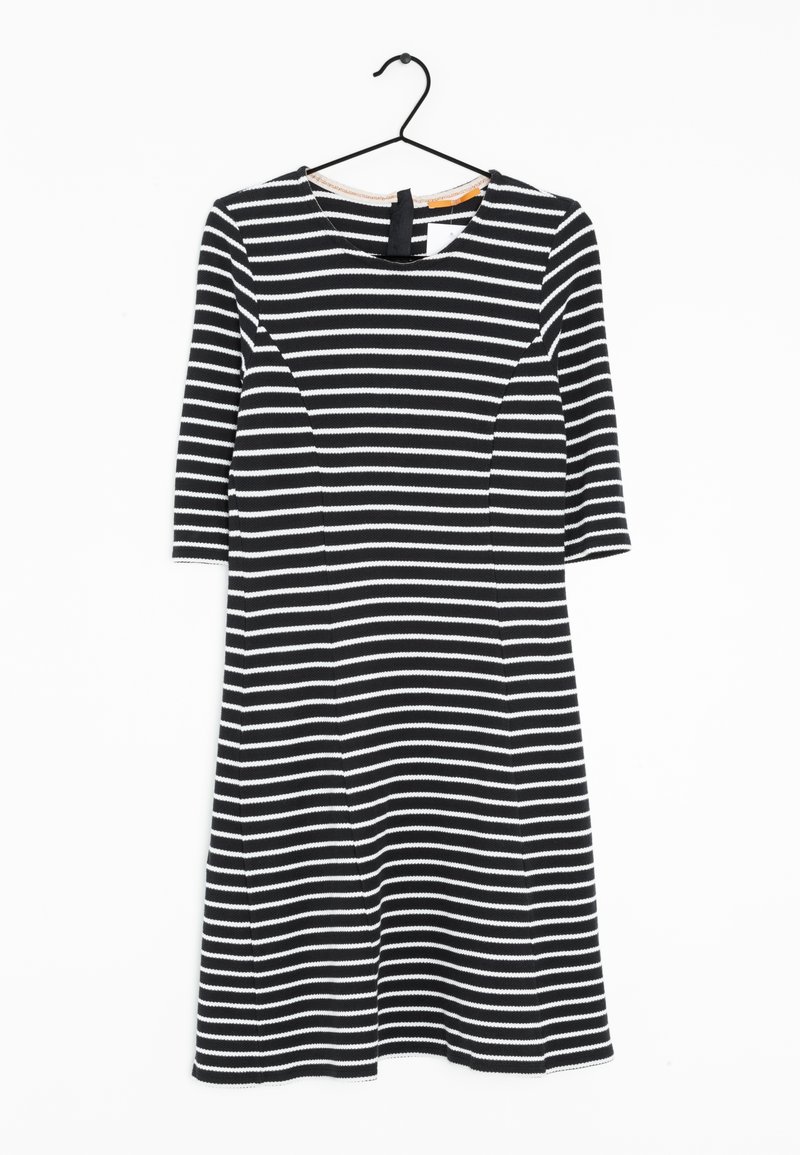 Robe à rayures horizontales noires et blanches avec des manches trois-quarts suspendue à un cintre noir sur un fond blanc.