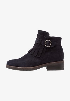 Mid-height navy suede ankle boot featuring a strap with a silver buckle and fringe detail. Low stacked heel and textured sole.