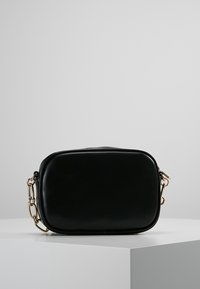 Černá kožená crossbody taška obdélníkového tvaru, s hladkým povrchem, zlatými detaily a řetízkem jako akcentem.