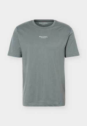 T-shirt uni vert pâle à col rond et manches courtes, avec petit logo blanc "Marc O’Polo" et texte centré sous l'encolure.