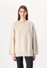 Pusero paksusta neuleesta, beige, jossa on letittimiä ja timanttikuvioita, pyöreä pääntie sekä ribbineulotut hihansuut ja helma; rento istuvuus ja teksturoitu pinta.