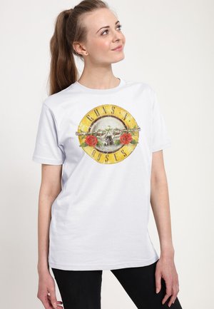 Ung kvinde med langt brunt hår i en hestehale iført en hvid Guns N' Roses T-shirt, der kigger op og mod hendes højre.