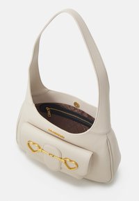 Krämfärgad läderaxelväska med framficka, guld hjärtformat spänne och brunt zip-foder på insidan.