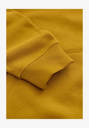 Geel sweatstof met geribbelde manchetten. Zachte textuur, aansluitend ontwerp en gelijkmatige stikseldetails.