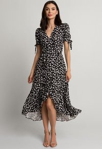 Czarna sukienka o kroju kopertowym z białym kwiatowym wzorem, z krótkimi puff-sleeve'ami, wiązaniem w talii, rozkloszowanym dołem i nieco dłuższym tyłem. Materiał wydaje się lekki.