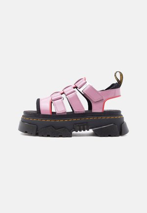 Sandala s debelim crnim potplatom i debelim ružičastim kožnim remenima, tri prednja zatvarača na čičak i crno-žuti izvlačni jezičak na peti.