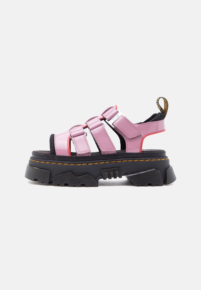 Σανδάλι με χοντρή μαύρη σόλα, χοντρές ροζ δερμάτινες λουρίδες, τρία μπροστινά κλείστα βέλκρο και μαύρη-κίτρινη θηλιά για τράβηγμα στη φτέρνα.