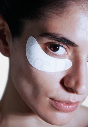 Patch idrogel per gli occhi applicato sotto l'occhio sinistro, materiale traslucido con testo in rilievo "FaceD"; pelle liscia, occhio marrone parzialmente visibile.