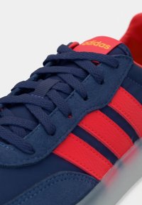 Plavi i crveni tenisice od tekstilnih i sintetičkih materijala. Imaju crvene pruge, plave vezice i teksturirani gornji dio. Logo prikazan na jeziku. 