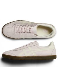 Light pink sneakers with a smooth leather upper, cream accents, round toe, and a textured brown rubber sole. Laces are flat and evenly spaced.
