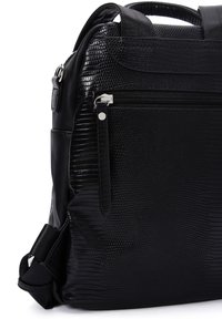 Sac à dos noir en matériau synthétique texturé, avec une poche avant zippée, une poignée supérieure et des bretelles réglables. Accentué par des éléments en métal argenté.